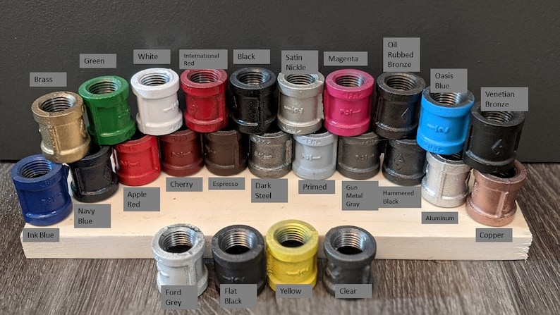 May include: A variety of colored metal pipe fittings, including brass, green, white, red, black, satin nickel, oil rubbed bronze, magenta, oasis blue, Venetian bronze, navy blue, ink blue, apple red, cherry, espresso, dark steel, primed, gun metal gray, hammered black, ford gray, flat black, yellow, and clear. The fittings are arranged in rows on a wooden surface.