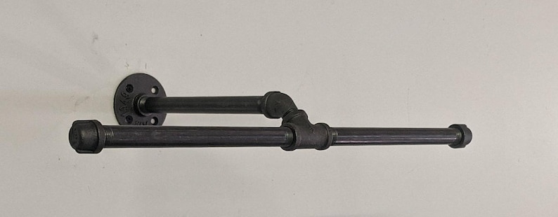 K&ouml;nnte beinhalten: Schwarzer Metall-Handtuchhalter mit zwei Stangen. Der Halter ist mit einer schwarzen Metallflansch an der Wand befestigt.