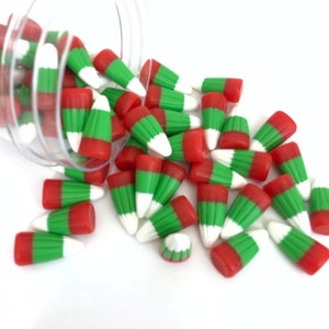 May include: A clear plastic jar filled with red and green candy corn. The jar is tipped over and the candy corn is spilling out onto a white surface.