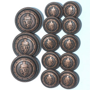 May include: Set of 10 copper-toned buttons with a raised design of a crown and shield. Each button has a rope-like border.
