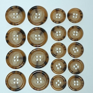 May include: A collection of 15 brown and black patterned buttons with four holes each.
