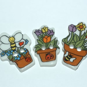 Peut inclure: Trois boutons en céramique avec un motif de pot de fleurs. Chaque bouton présente un arrangement floral différent, y compris une abeille, une coccinelle et un cœur. Les boutons sont blancs avec des accents bruns, jaunes, rouges et verts.