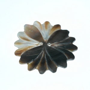 May include: A decorative button with a flower design. The button is made of a pearlescent material with shades of brown, tan, and black. It has two holes for sewing and a scalloped edge, resembling petals.