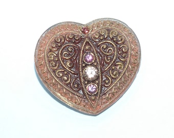 May include: Heart-shaped vintage jewelry box with ornate filigree design. The box features a copper-colored exterior with gold accents and is adorned with pink and clear gemstones. A small red gemstone is at the top.