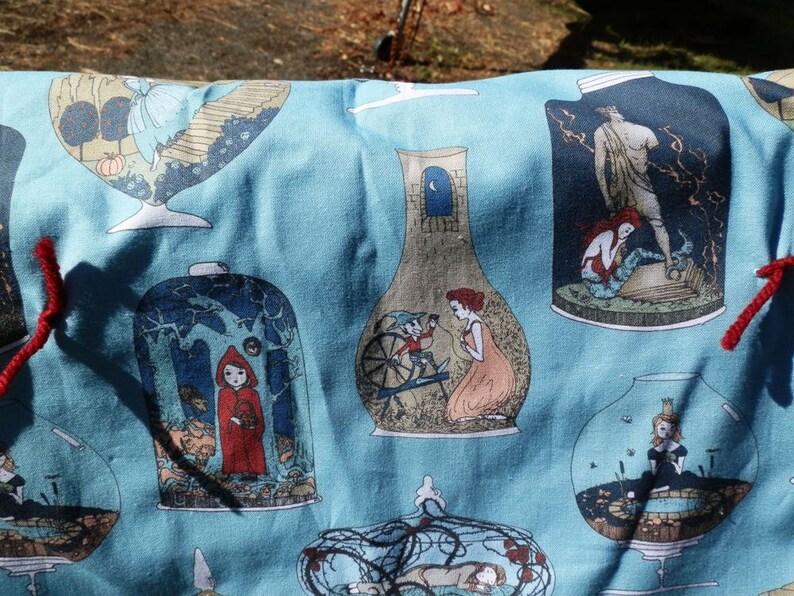 Pu&ograve; includere: Tessuto azzurro con illustrazioni ripetute di scene di fiabe all'interno di barattoli di vetro. Le illustrazioni includono Cappuccetto Rosso, sirene e altre figure fantastiche. I legami di filo rosso sono visibili sui bordi.