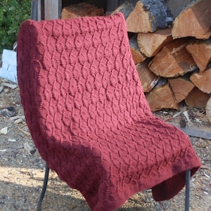 May include: A burgundy knitted throw blanket with a cable knit pattern draped over a metal chair.