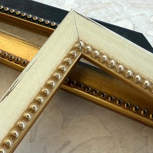 May include: Close-up of three picture frames in black, gold, and off-white. Each frame has a beaded edge. The frames are angled, showing their corners and the details of the decorative trim.