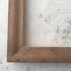 May include: A close-up of a wooden picture frame with a natural wood finish. The frame has a simple, rectangular design and a smooth surface.