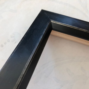 May include: Close-up of a black picture frame with a wood backing. The frame has a slightly distressed finish.