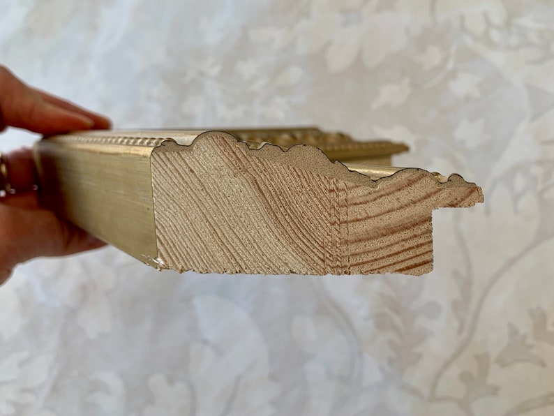 Pu&ograve; includere: Primo piano del lato di una cornice dorata. La cornice &egrave; in legno e ha un design decorativo e ornato.