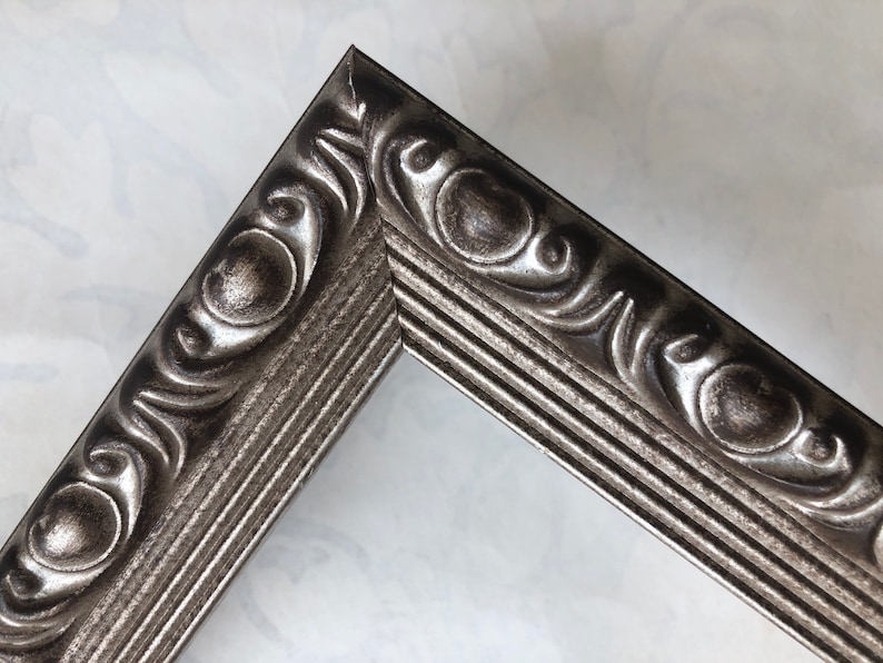 May include: Close-up of a silver picture frame with an ornate, raised design. The frame has a textured, metallic finish.
