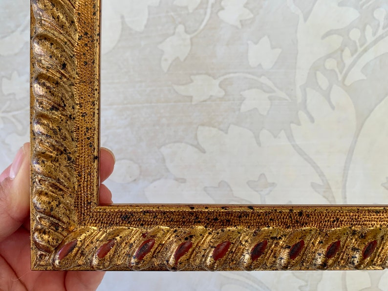 May include: A gold picture frame with a rope-like design and red accents. The frame has a distressed finish.