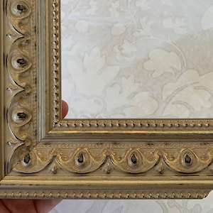 Pu&ograve; includere: Primo piano di una cornice dorata con dettagli decorativi. La cornice ha una finitura usurata e un bordo perlato.