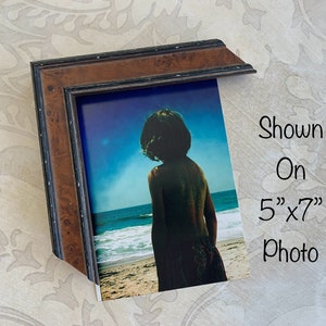 May include: A brown wood picture frame with a black inner border. The frame is shown with a 5" x 7" photo of a person standing on a beach.