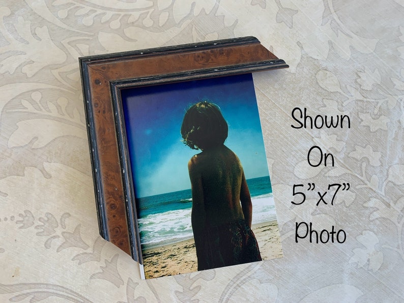May include: A brown wood picture frame with a black inner border. The frame is shown with a 5" x 7" photo of a person standing on a beach.