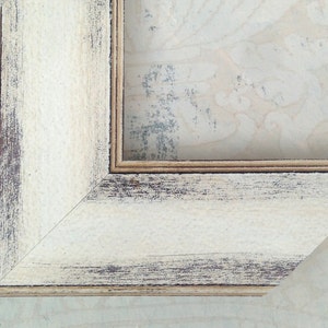 May include: Close-up of a corner of a white wooden picture frame with a distressed finish. The frame has a double border and a slightly raised edge.