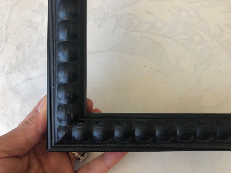 May include: Close-up of a black picture frame with a beaded edge. The frame is made of wood and has a smooth finish.