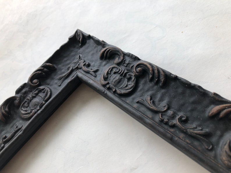 May include: Black ornate picture frame with a textured surface and intricate details. The frame is made of wood and has a dark finish.