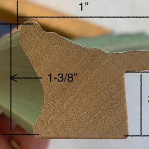 May include: Close-up of a section of a green picture frame molding. The frame is 1 inch wide, 1-3/8 inches deep, and 3/4 inch high. The frame has a decorative edge and a natural wood-colored interior.