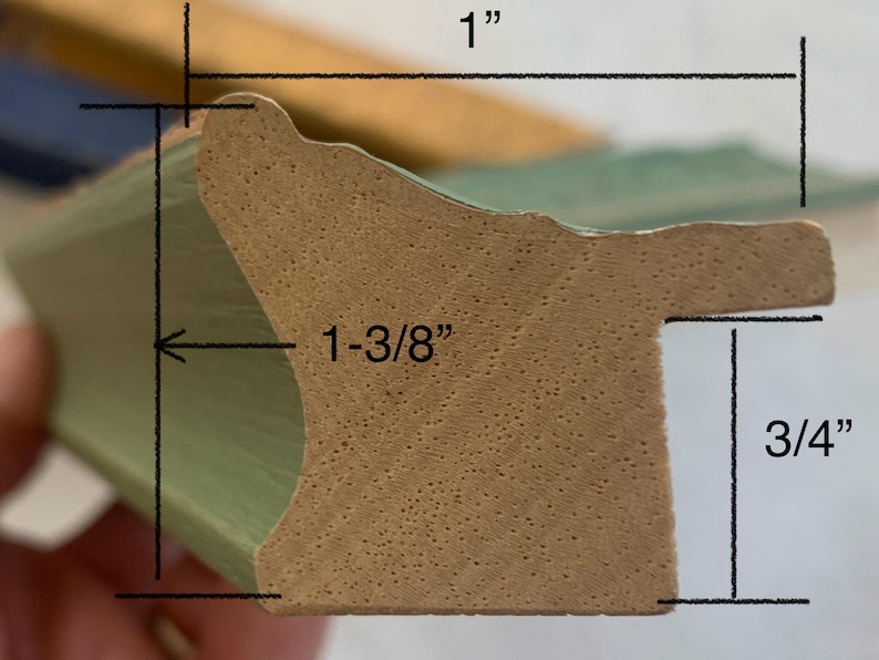 May include: Close-up of a section of a green picture frame molding. The frame is 1 inch wide, 1-3/8 inches deep, and 3/4 inch high. The frame has a decorative edge and a natural wood-colored interior.