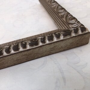 May include: A close-up of a silver picture frame with an ornate design. The frame has a distressed finish, giving it a vintage look.