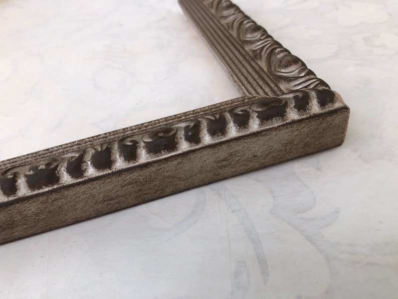 May include: A close-up of a silver picture frame with an ornate design. The frame has a distressed finish, giving it a vintage look.