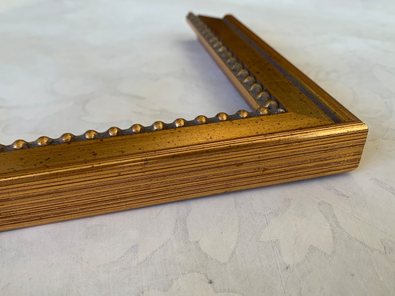 May include: A gold picture frame with a beaded edge and a wood grain finish.