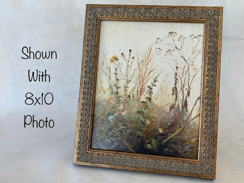 May include: A gold-toned picture frame with an ornate design. The frame is shown with an 8x10 photo of a dried flower arrangement.