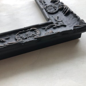 May include: A black ornate picture frame with a detailed, raised design. The frame is made of wood and has a distressed finish.