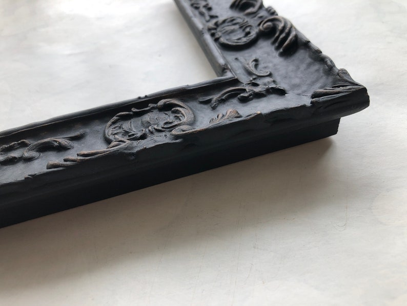 May include: A black ornate picture frame with a detailed, raised design. The frame is made of wood and has a distressed finish.