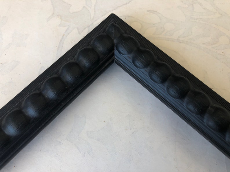 May include: Close-up of a black picture frame with a beaded edge. The frame is made of wood and has a smooth finish.
