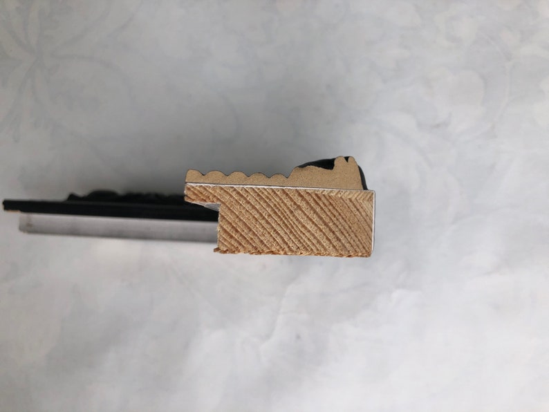 K&ouml;nnte beinhalten: Nahaufnahme der Seite eines schwarzen Bilderrahmens mit einem Holzkern. Der Holzkern hat eine hellbraune Farbe und ein diagonales Maserungsmuster.