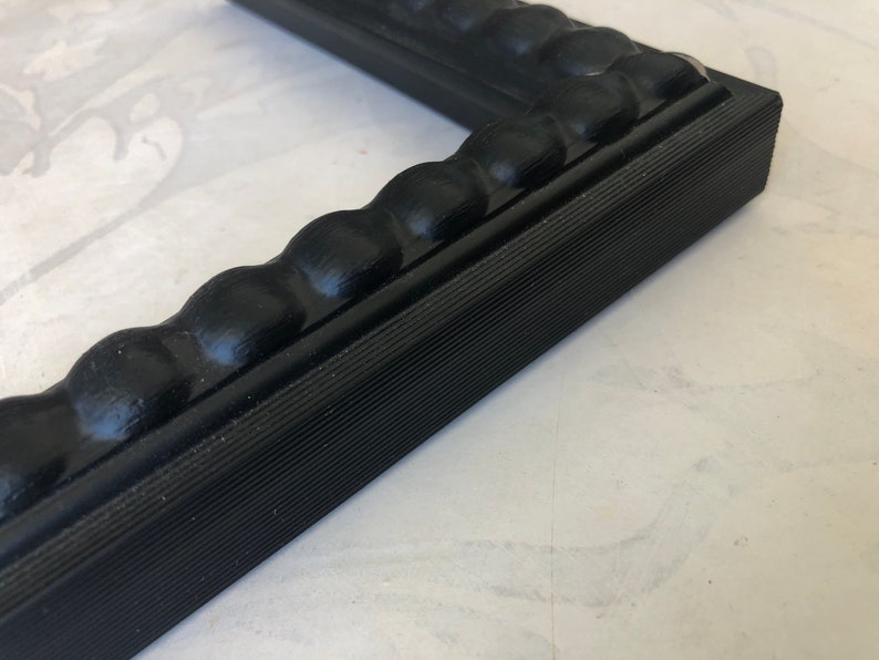 May include: Black picture frame with a beaded edge and a textured surface.