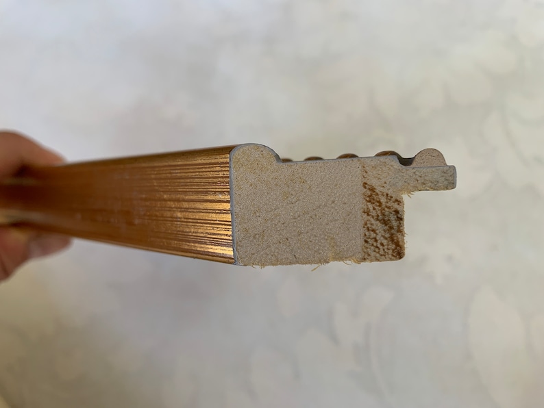 May include: Close-up of the side of a gold picture frame. The frame is made of wood and has a decorative edge.