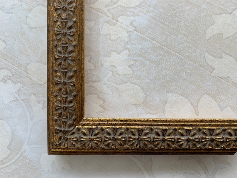 May include: A gold picture frame with a decorative, ornate design. The frame has a raised edge and a detailed pattern.