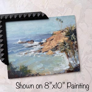May include: An 8"x10" painting of a coastal scene with a black frame. The artwork depicts a rocky cliff, ocean waves, and a light blue sky. The painting has a textured, impressionistic style.