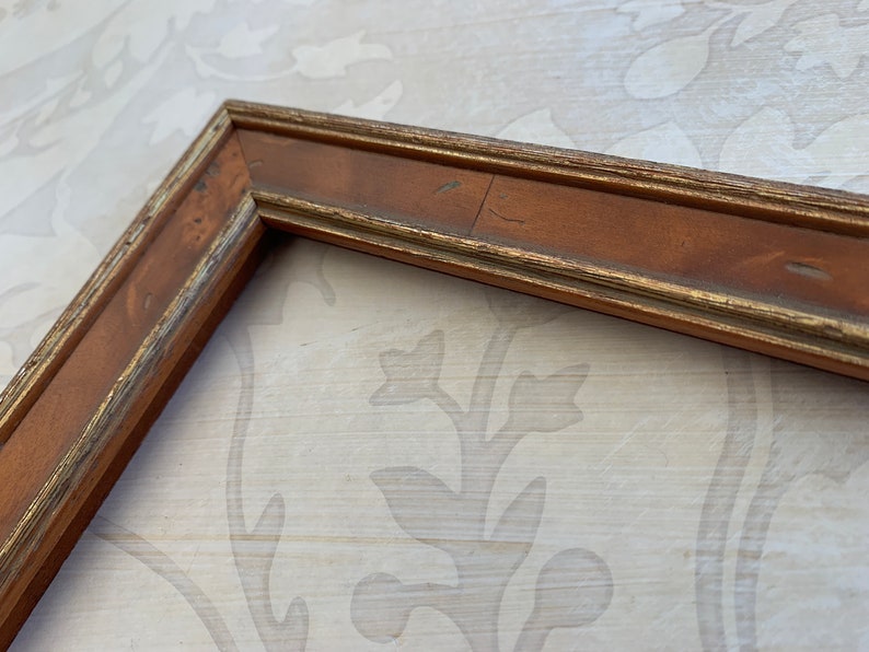 May include: A wooden picture frame with a gold trim. The frame is brown and has a distressed look.