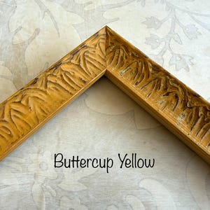 May include: A corner of a buttercup yellow picture frame with carved leaf-like details. The frame has a distressed finish, and the text "Buttercup Yellow" is written in a black script font.