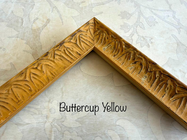 May include: A corner of a buttercup yellow picture frame with carved leaf-like details. The frame has a distressed finish, and the text "Buttercup Yellow" is written in a black script font.