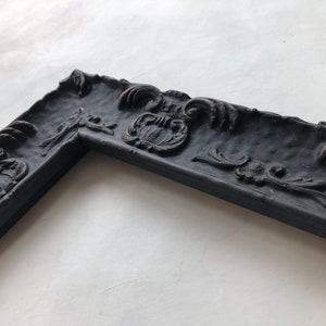 May include: A black ornate picture frame with a detailed, textured design. The frame has a slightly distressed look, adding to its vintage charm.