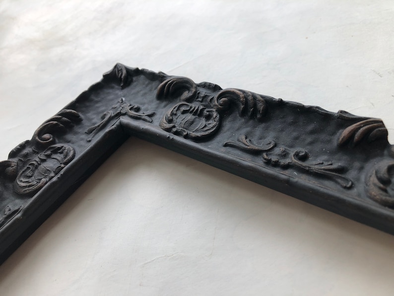 May include: A black ornate picture frame with a detailed, textured design. The frame has a slightly distressed look, adding to its vintage charm.