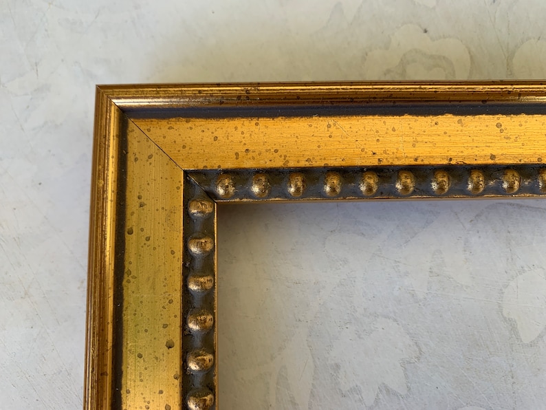 May include: Close-up of a gold picture frame with a beaded edge. The frame has a distressed finish and is made of wood.
