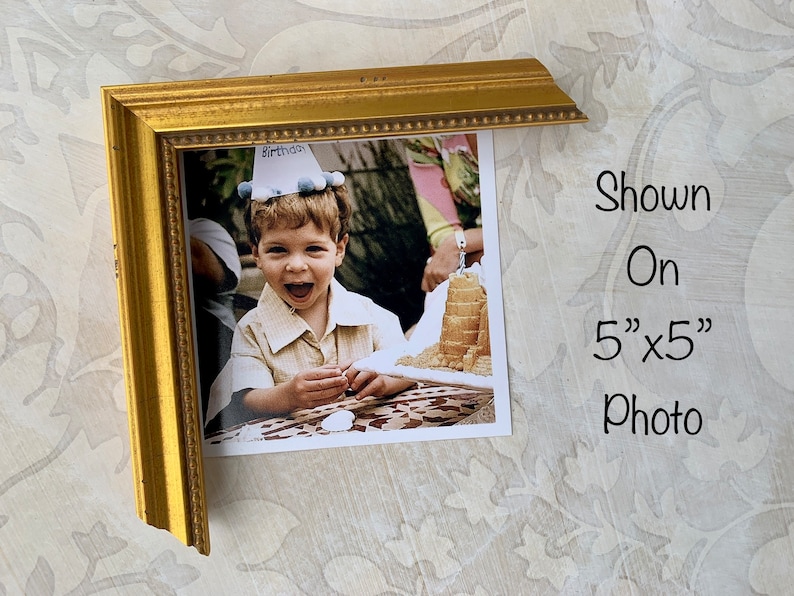 Puede incluir: Un marco de fotos dorado con una foto de 12,7 cm x 12,7 cm de un ni&ntilde;o peque&ntilde;o con un gorro de cumplea&ntilde;os. El ni&ntilde;o sonr&iacute;e y sostiene un trozo de pastel. La foto est&aacute; sobre un fondo blanco.