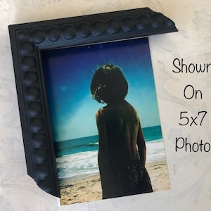 May include: Black picture frame with a beaded edge, shown on a 5x7 photo of a person standing on a beach.