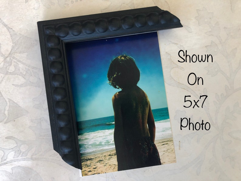 May include: Black picture frame with a beaded edge, shown on a 5x7 photo of a person standing on a beach.