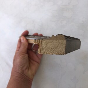 May include: Close-up of the side of a picture frame. The frame is made of wood and has a dark brown finish. The wood is visible on the inside of the frame.