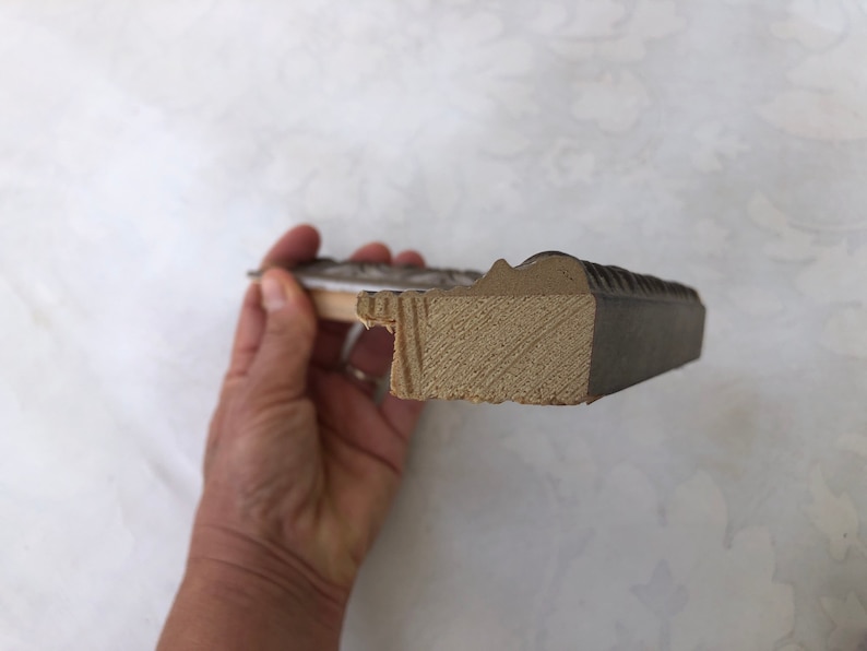 May include: Close-up of the side of a picture frame. The frame is made of wood and has a dark brown finish. The wood is visible on the inside of the frame.