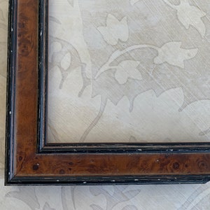May include: A close-up of a brown wood picture frame with a black trim. The frame has a beveled edge and a slightly distressed finish.