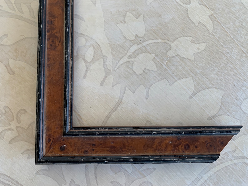 May include: A close-up of a brown wood picture frame with a black trim. The frame has a beveled edge and a slightly distressed finish.