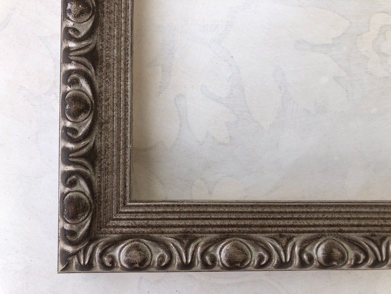 May include: A silver picture frame with an ornate design. The frame has a raised edge and a decorative border.